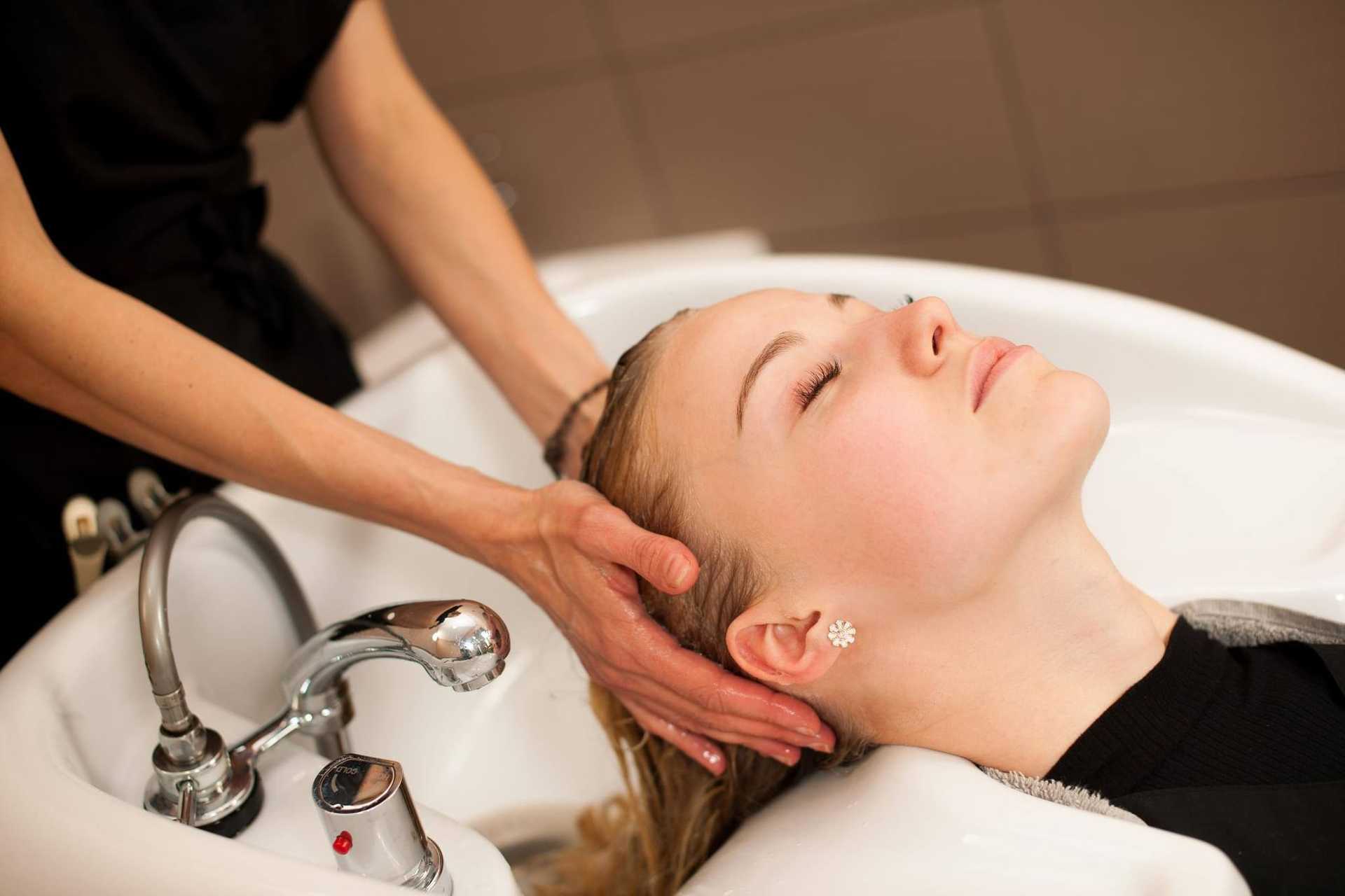 Person getting hair washed at a salon sink, hands of stylist gently massaging head.
