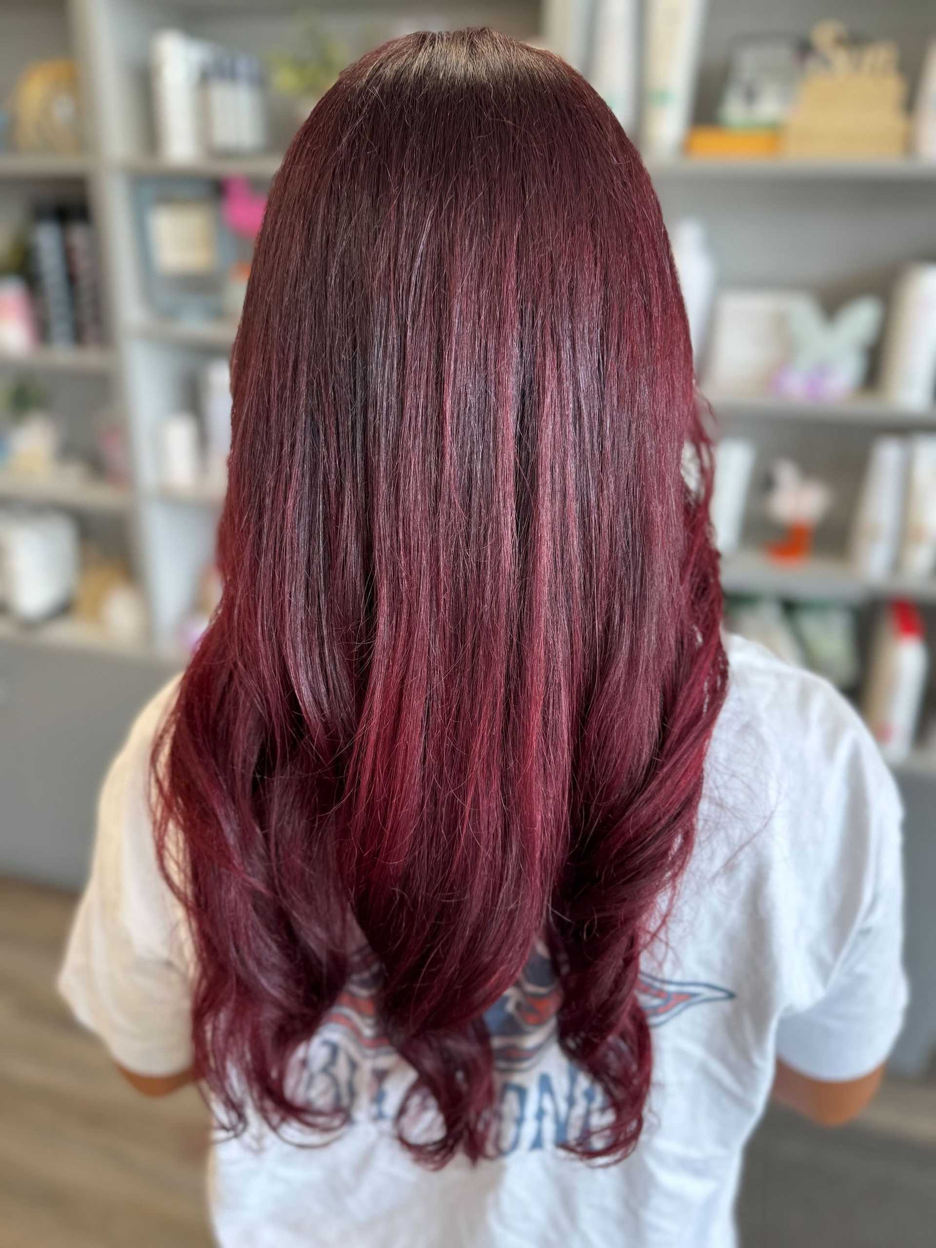 Red ombre hair with soft curls, viewed from the back in a salon setting.