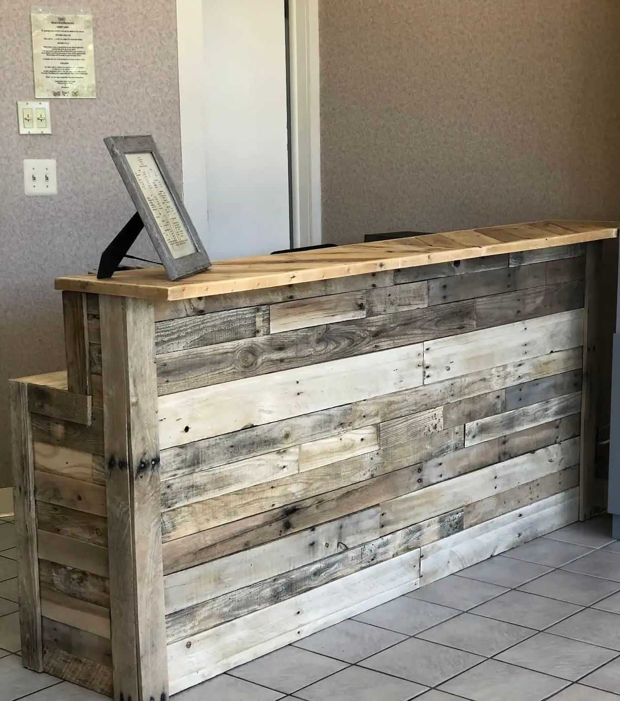 Rustic wooden reception desk in a tiled room with framed document on top.