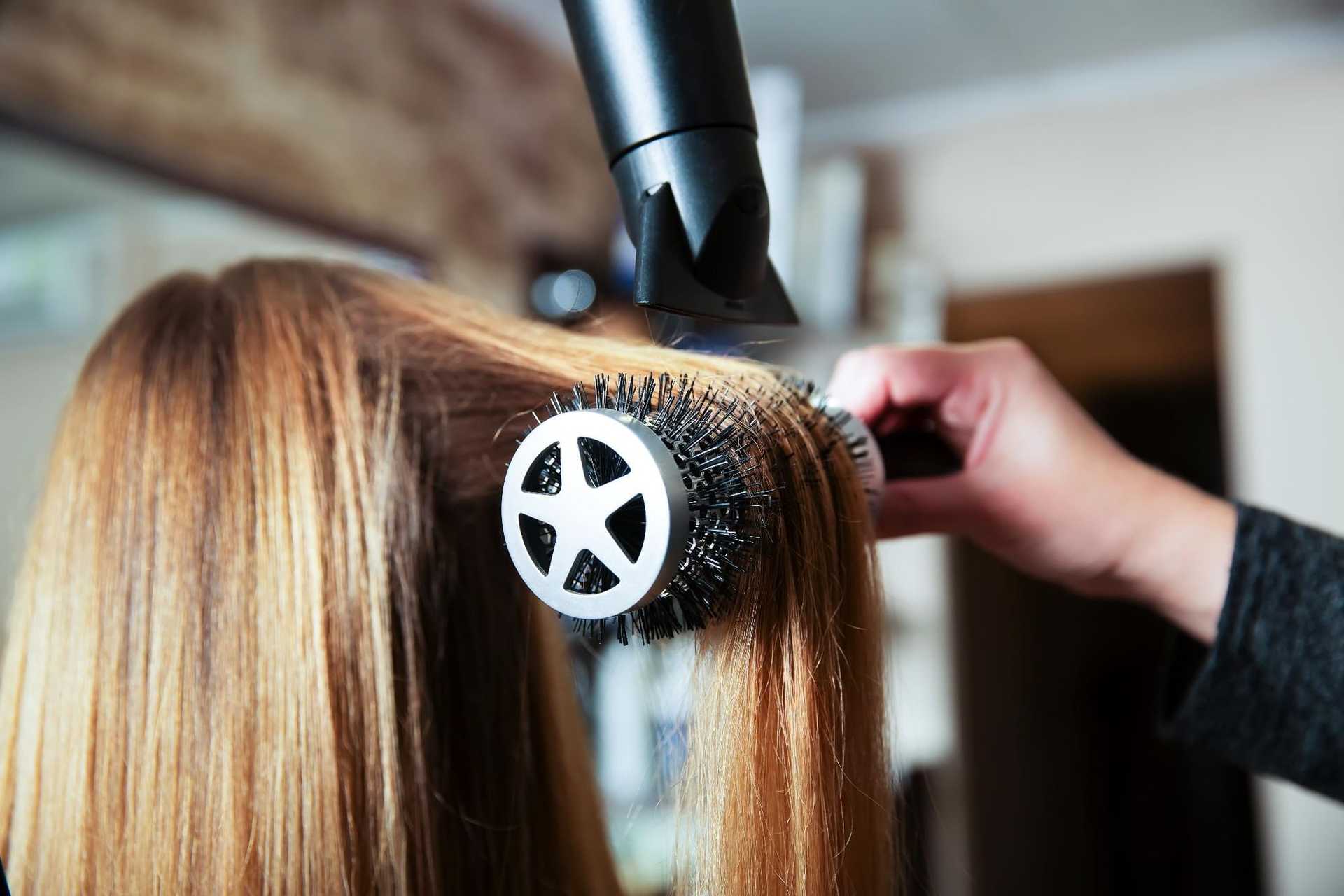 Hair being styled with a round brush and hair dryer in a salon setting.