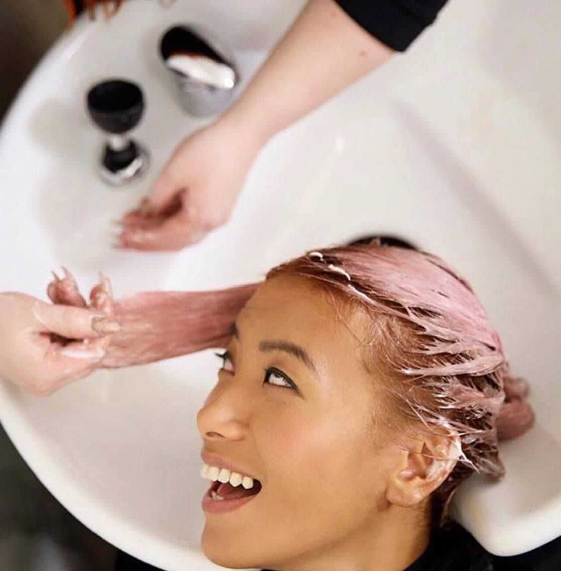 Person enjoying hair wash with pink dye in salon sink.